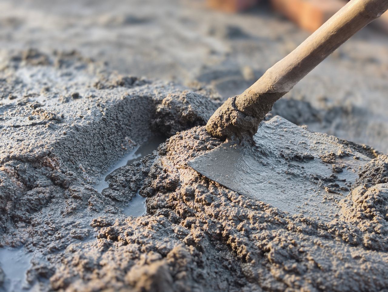 Detailed image of a shovel mixing wet cement, showcasing construction work.